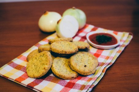 Baked Round Cookie Beside Red Sauce With Green Toppings photo