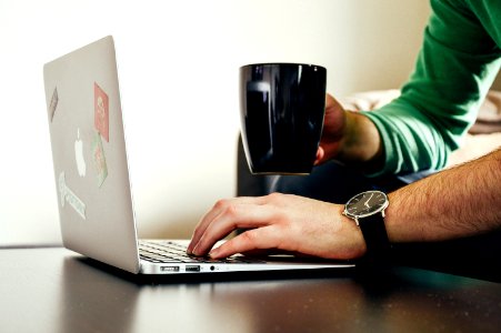 Person Wearing Green Long Sleeve Shirt Holding Black Ceramic Mug And Macbook Air