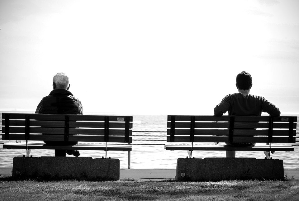 Grayscale Photo 2 Person Sitting In A Separate Benches On The Seaside