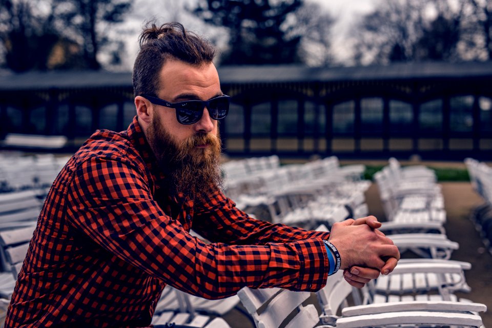 Man Wearing Black And Red Checkered Long Sleeve Shirt Wearing Black Wayfarer Sunglasses Sitting On White Wooden Chair photo