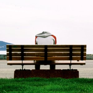 Person Wearing Grey And Orange Hoodie Sitting On Brown Wooden Park Bench During Daytime photo