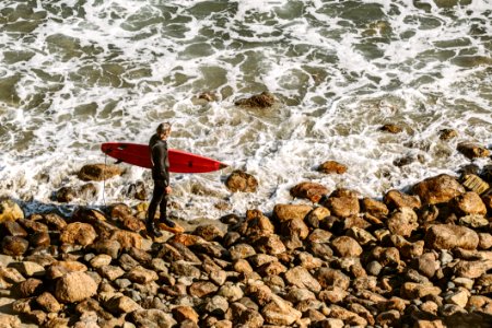 Man Wearing Wetsuit And Holding Red Surfboard On Shore photo