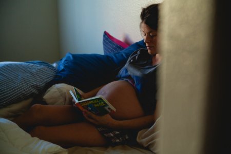 Pregnant Woman Sitting On Bed And Reading Book photo