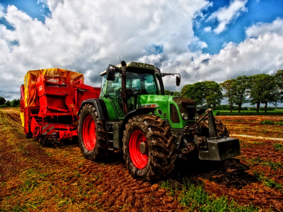 Green Tractor Pulling Red Bin On Field At Daytime