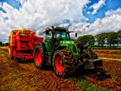 Green Tractor Pulling Red Bin On Field At Daytime