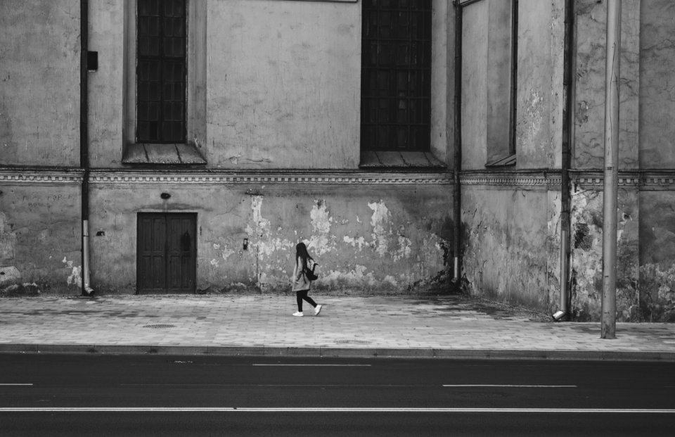 Gray Scale Photography Of Woman Walking Near High Rise Building