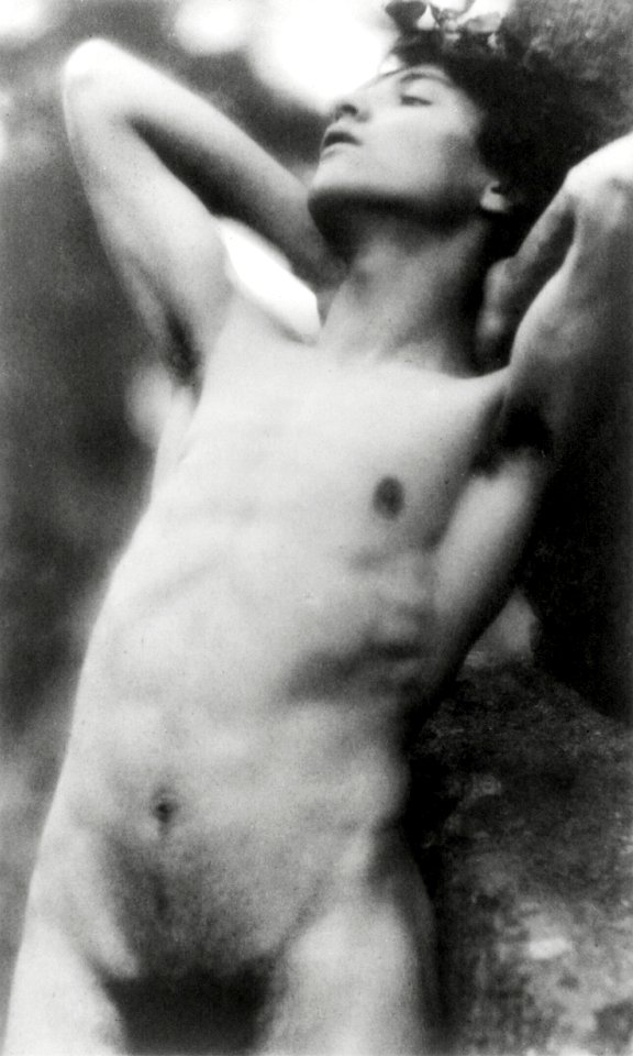 Nude photography of naked man: Portrait Photograph of nude youth with laurel wreath against rock with hands behind neck, cropped at thighs (1907) by Fred Holland.