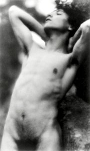 Nude photography of naked man: Portrait Photograph of nude youth with laurel wreath against rock with hands behind neck, cropped at thighs (1907) by Fred Holland. photo