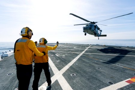 On the top deck of the USS San Diego, U.S. Navy personnel monitor a helicopter landing after an Orion underway recovery test.