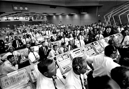 Members of the Kennedy Space Center government-industry team rise from their consoles within the Launch Control Center to watch the Apollo 11 liftoff through a window.