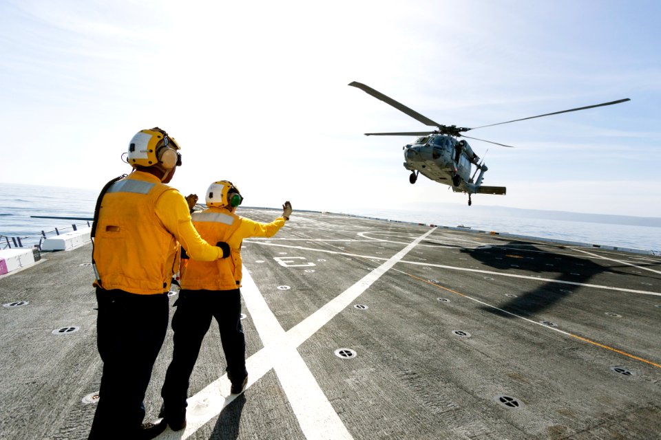 On the top deck of the USS San Diego, U.S. Navy personnel monitor a helicopter landing.