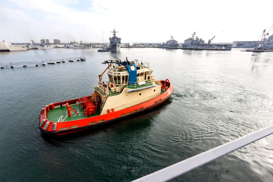 At the U.S. Naval Base San Diego in California, a tug boat accompanies the USS San Diego as it departs for open seas in the Pacific Ocean.