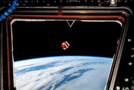 A dice floating in front of one of the windows in the Cupola of the Earth-orbiting International Space Station.