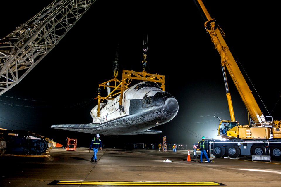 The space shuttle Discovery suspended from a sling held by two cranes.