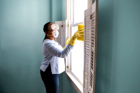 Woman using a damp sponge to clean dust collected on a window sill. Original image sourced from US Government department: Public Health Image Library, Centers for Disease Control and Prevention. Under US law this image is copyright free, please credit the government department whenever you can”. photo