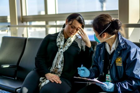 A healthcare worker assessing a sick traveler at the airport. Original image sourced from US Government department: Public Health Image Library, Centers for Disease Control and Prevention. Under US law this image is copyright free, please credit the government department whenever you can”.