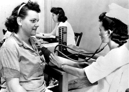 The 1950s historical photograph of a nurse taking her blood pressure of a woman ordnance worker in the hospital. Original image sourced from US Government department: Public Health Image Library, Centers for Disease Control and Prevention. Under US law this image is copyright free, please credit the government department whenever you can”.