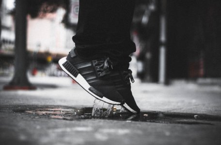 Grayscale Photo Of Person Wearing Adidas Nmd Jumping On Puddle