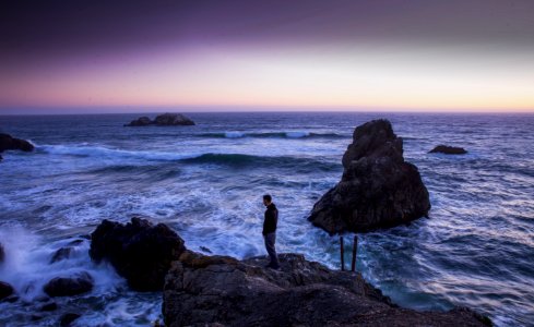 Man In Black Shirt Standing On Rock In Between Sea Water photo