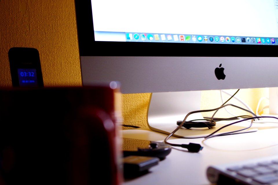 Silver Imac Turned On Beside Red Ceramic Cup