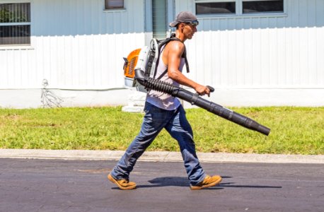 Man In White Tank Top And Blue Denim Pants With Leaf Blower Outdoors During Daytime photo