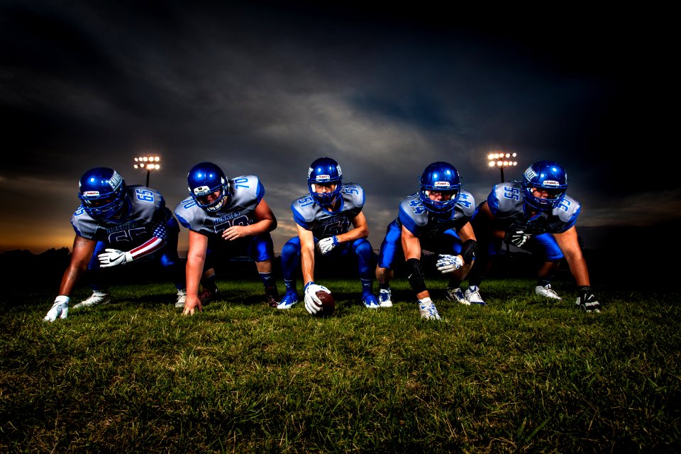 Football Players In Blue Jersey Lined Under Grey White Cloudy Sky During Sunset