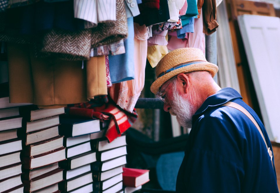 Man In Brown Sun Hat Facing Black Covered Piled Books