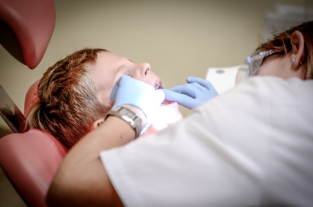 Dentist Woman Wearing White Gloves And White Scrubsuit Checking Boys Teeth photo