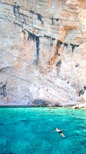 Man In Blue Waters Along Cliff