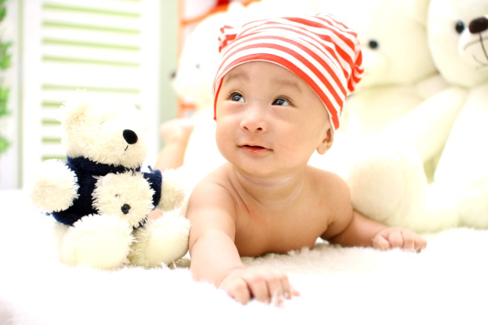 Smiling Toddler Wearing Orange And White Knit Cap Beside Black And White Bear Plush Toy