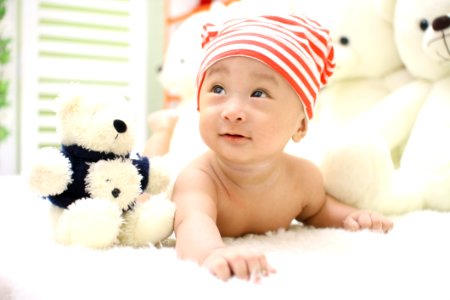 Smiling Toddler Wearing Orange And White Knit Cap Beside Black And White Bear Plush Toy photo