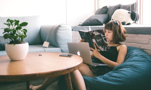 Woman Sitting On Bean Bag White Using Macbook In Front Of Round Table With Green Leafed Plant