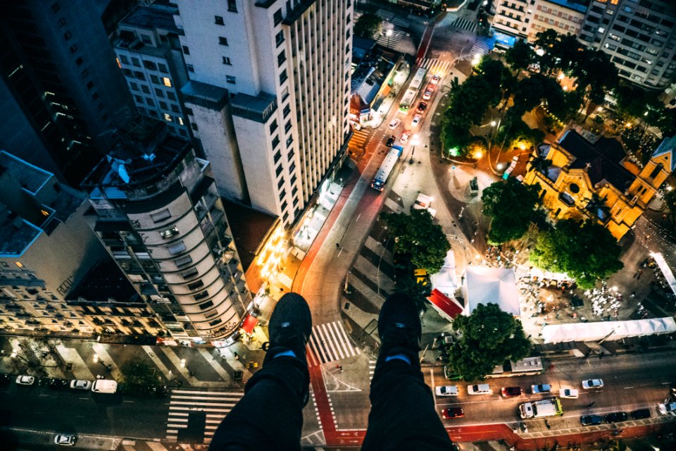 Man Sitting On High Rise Building Taking Photo Below