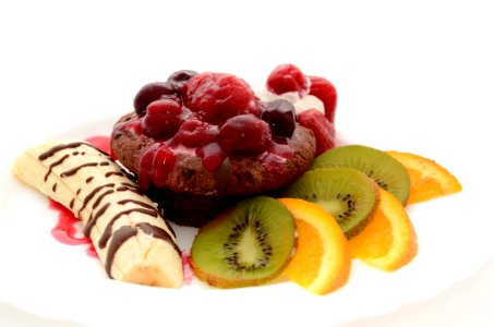 Banana Drizzled With Chocolate Syrup Beside Chocolate Cupcake With Raspberry And Kiwi And Orange Slices On The Side On White Plate photo