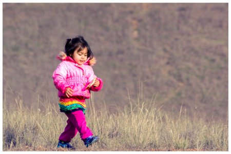 Woman In Pink Down Jacket Walking On Green Grass During Daytime photo