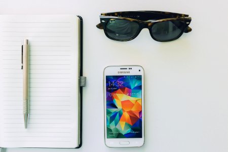 White Samsung Smartphone Beside Sunglassespen And White Notebook photo