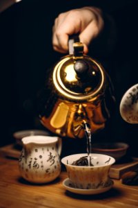 Person Holding Gold Teapot Pouring White Ceramic Teacup photo