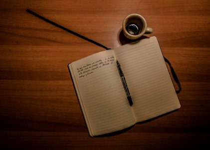Pen On Notebook Beside A Teacup On Brown Wooden Plank photo