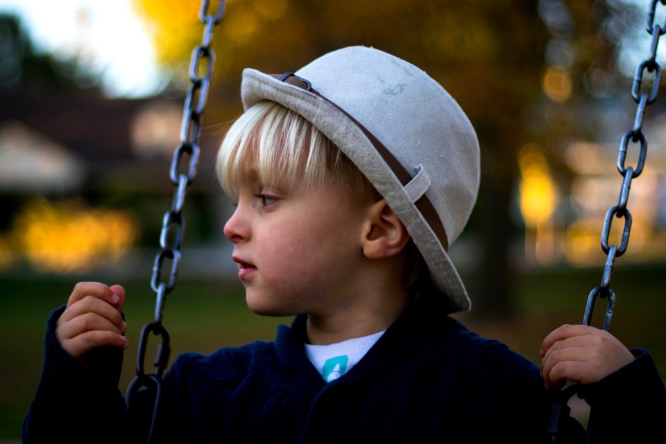 Kid In Gray Round Hat On Hanging Swing
