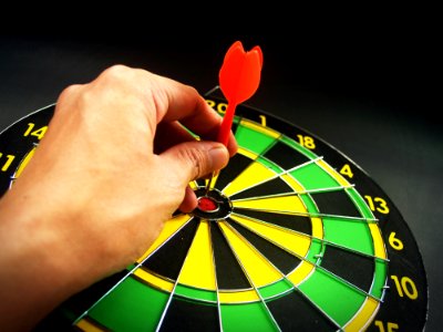 Person Holding Red Dart On Green Yellow And Black Dart Board photo