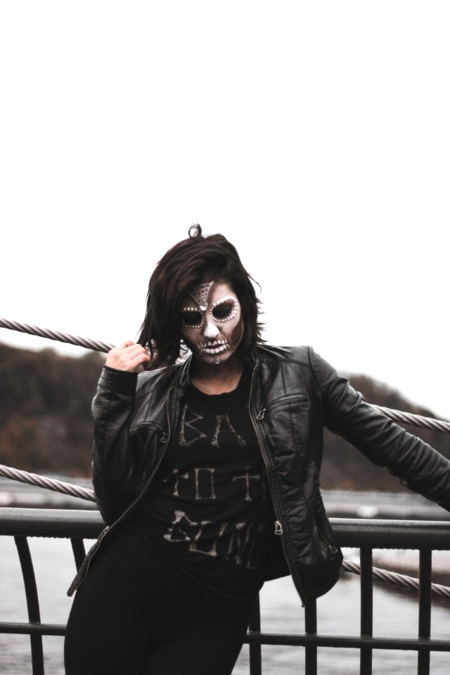 Woman Wearing Gray Halloween Mask And Black Leather Jacket Standing By Black Railings photo