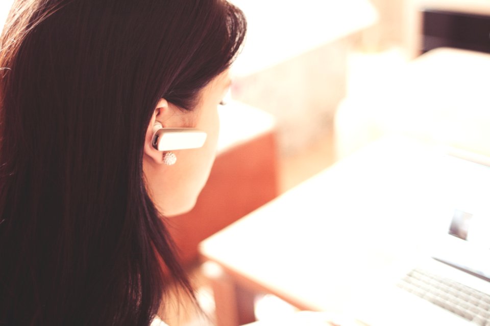 Woman Wearing Earpiece Using White Laptop Computer