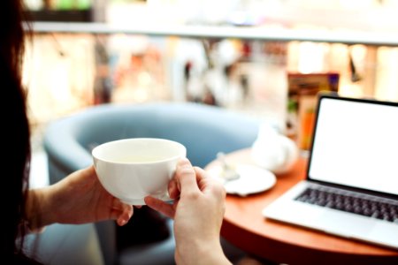 Person Holding White Ceramic Teacup In Front Of A Macbook Pro photo
