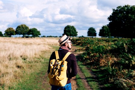 Man With Backpack Walking On Pathway Between Field At Daytime photo