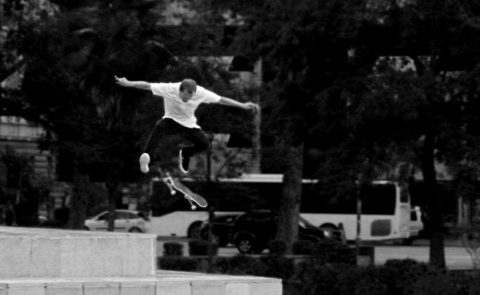 Man In White Shirt And Black Pants Playing Skateboard Near Green Tree During Daytime photo