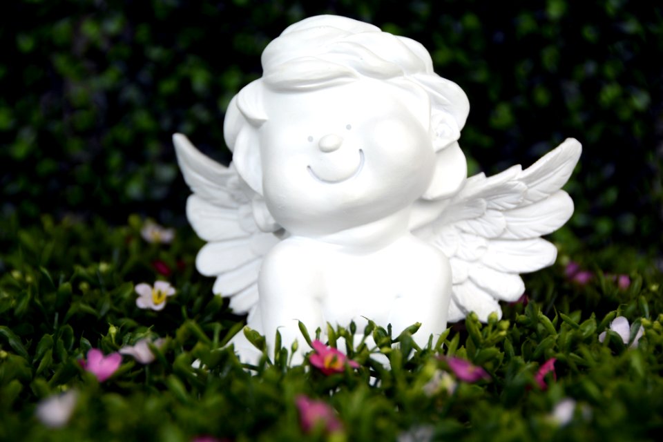 White Angel Ceramic Figurine On Green Grass With White And Purple Flower