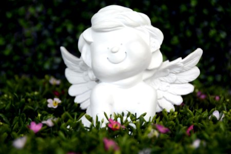 White Angel Ceramic Figurine On Green Grass With White And Purple Flower photo