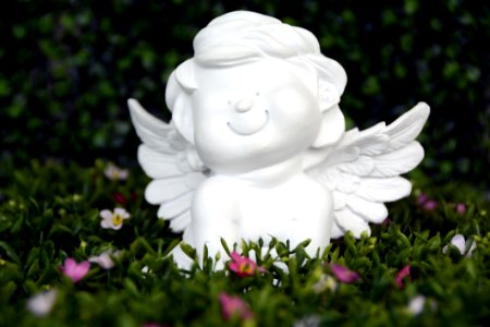 White Angel Ceramic Figurine On Green Grass With White And Purple Flower