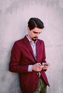 Man Wearing Maroon Blazer Leaning On Gray Concrete Wall While Using His Smartphone