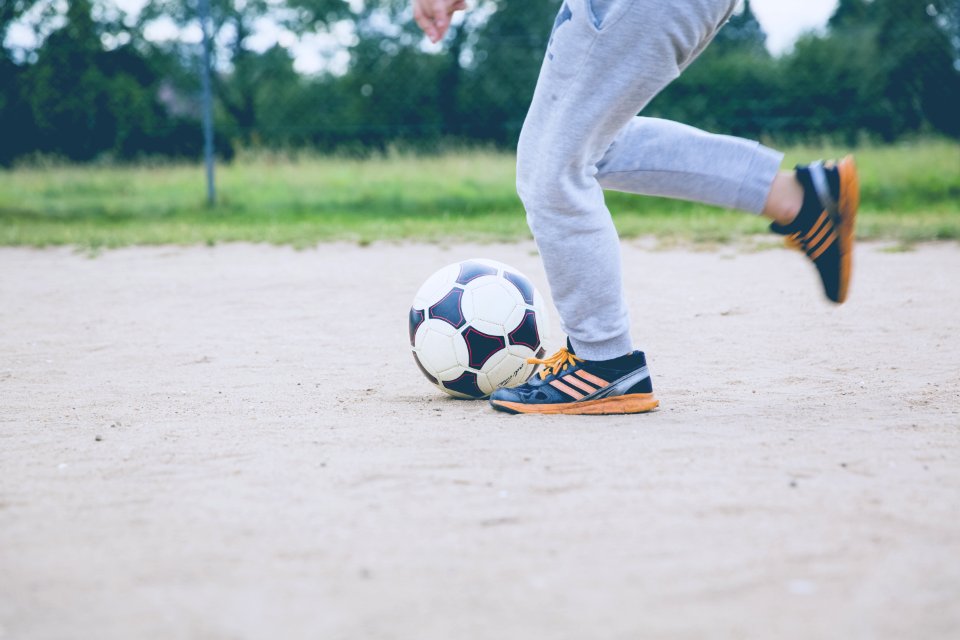 Person Kicking Soccer Ball On Gray Sand